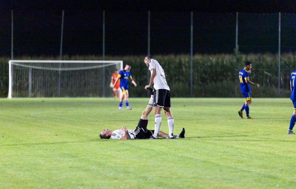 Ein Spieler des SV Miesbach liegt mit Krampf auf dem Rasen, ein Mitspieler dehnt ihm das Bein