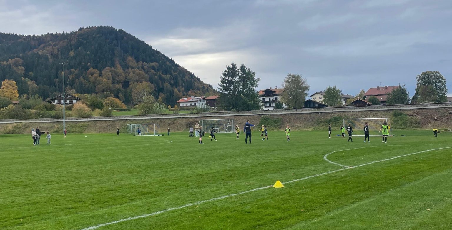 Spielfeld in Schliersee mit Kindern beim Aufwärmen, im Hintergrund ein bewaldeter Berg