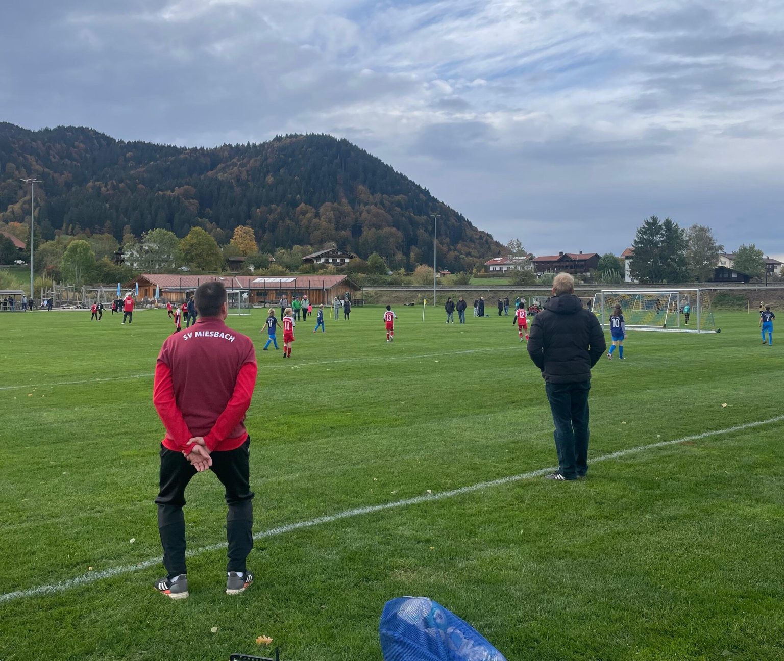 Trainer des SV Miesbach an der Seitenlinie, dahinter Kinder beim Spiel auf dem Rasen in Schliersee