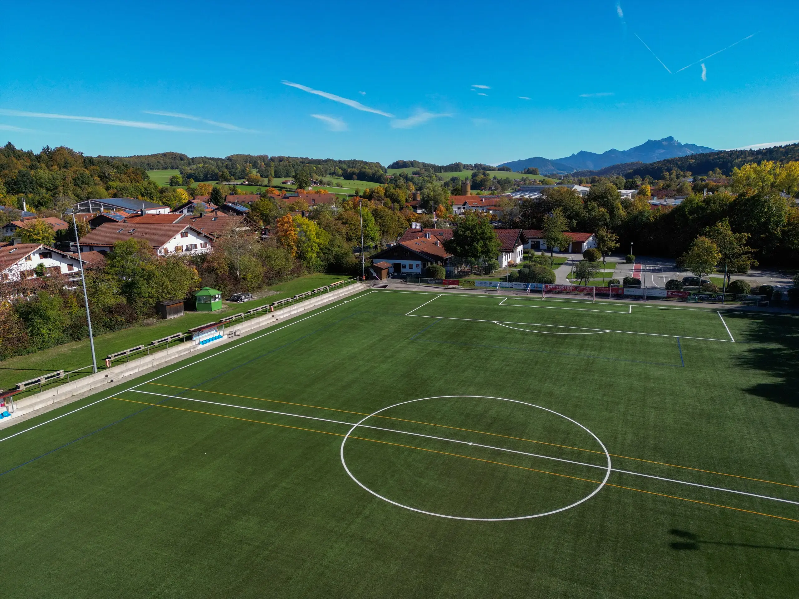 Kunstrasenplatz der Senator-Voigt-Sportanlage aus der Luft, dahinter die Berge