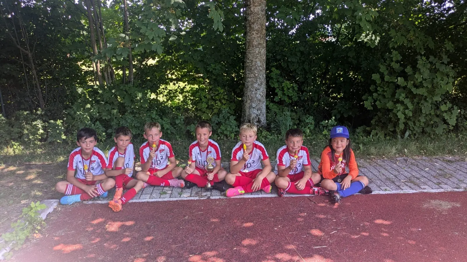 Die F-Jugend des SV Miesbach sitzt mit Pokal und Medaillen im Schatten – Teamfoto nach dem Turnier in Wall